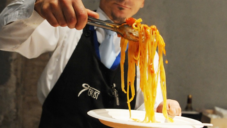 A waiter preparing a serving of spaghetti with amatriciana sauce