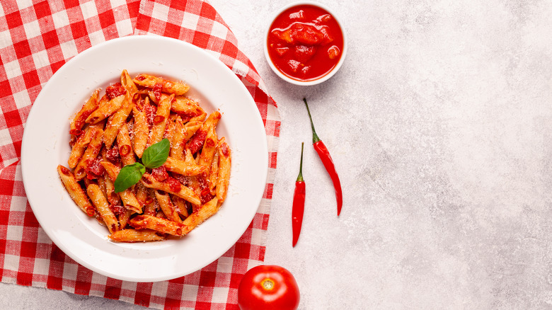 Penne with fresh basil and arrabbiata sauce on a checkered tablecloth by chili peppers