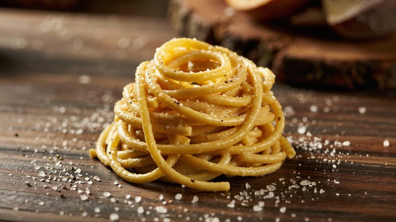Pici with cacio e pepe sauce and parmesan on a wooden slate
