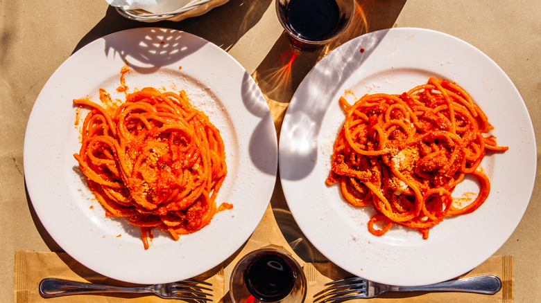 Two plates of pasta with pomodoro sauce by two forks and glasses of red wine.