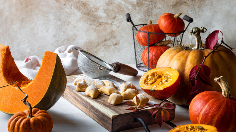 Uncooked pumpkin gnocchi on a wooden board surrounded by pumpkins of various sizes