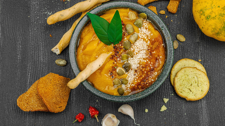 A bowl of pumpkin hummus on a gray background with crackers