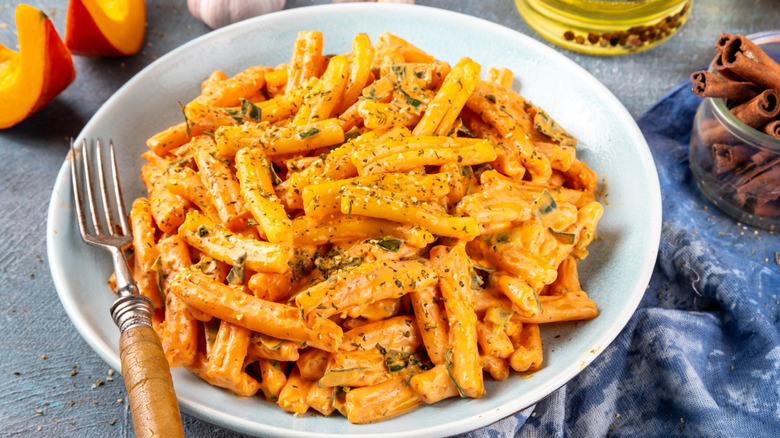 A bowl of creamy pumpkin mac and cheese on a table surrounded by pumpkin and spices