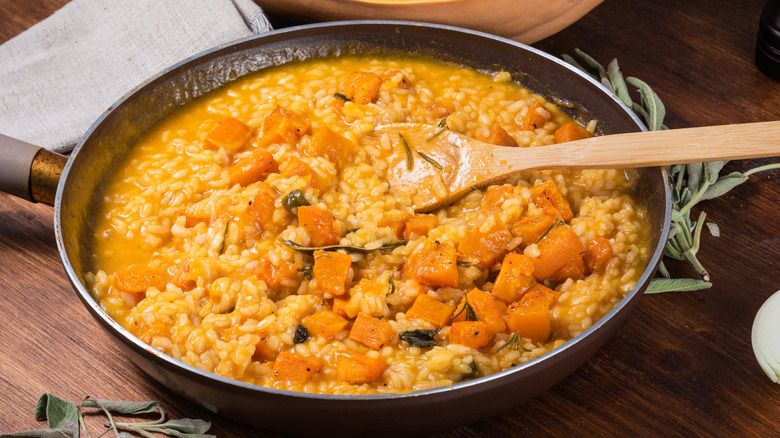 A bowl of pumpkin risotto with a wooden spoon on a wooden table