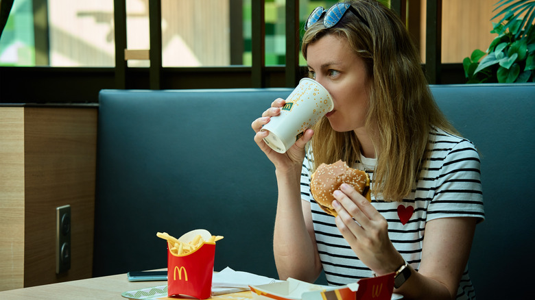 woman drinking soda and holding McDonald's burger