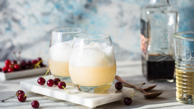 Two glasses of pale soda and ice cream in a float with cherries next to them