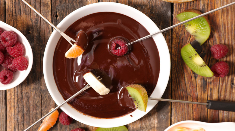 A raspberry, and slices of orange, banana, and kiwi dipped into Chocolate Fondue