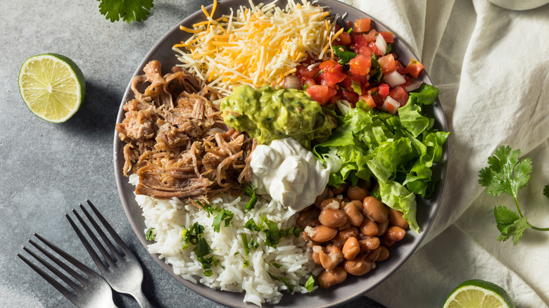 a carnitas burrito bowl with cheese, veggies, and rice