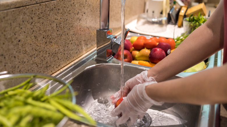 rinsing vegetable in sink with gloves