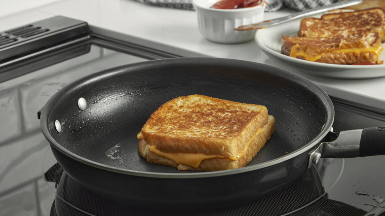 Grilled cheese cooks in a pan on a stove with other sandwiches plated nearby.