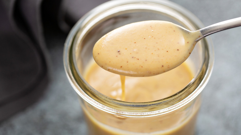 spoon scooping yellow-hued salad dressing out of glass jar