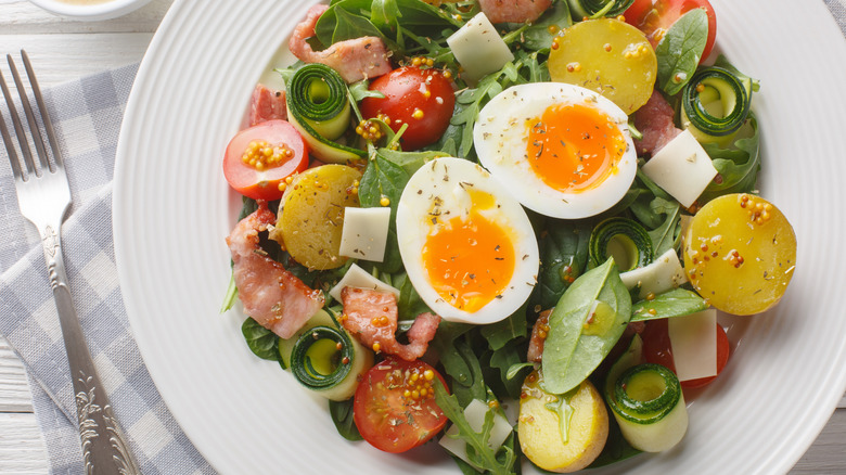 plate full of dressed salad with bacon, tomatoes, and eggs