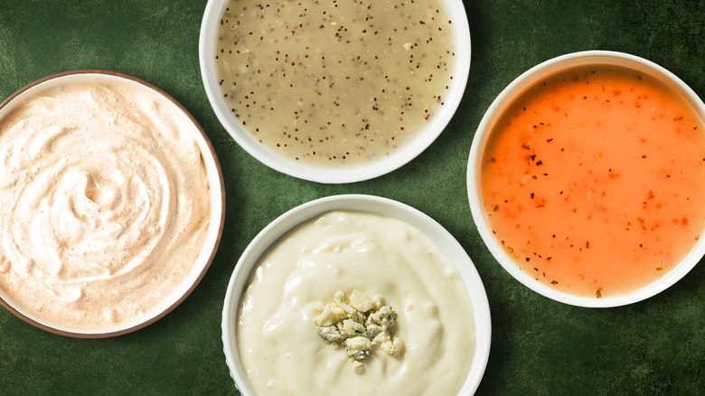 four white bowls of salad dressing against green background