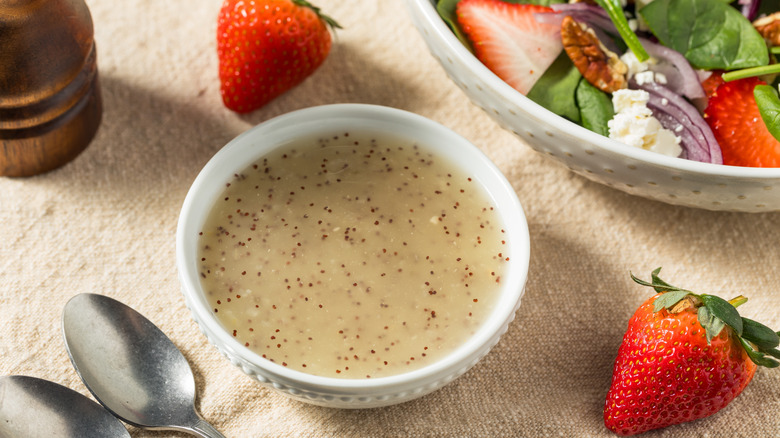 small white dish filled with poppy seed dressing surrounded by strawberries and spoons