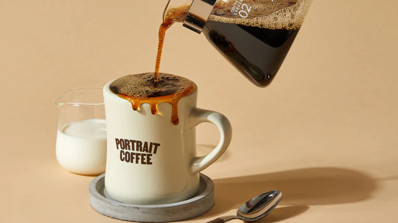 Filter coffee being poured into an overflowing mug next to a cup of coffee creamer