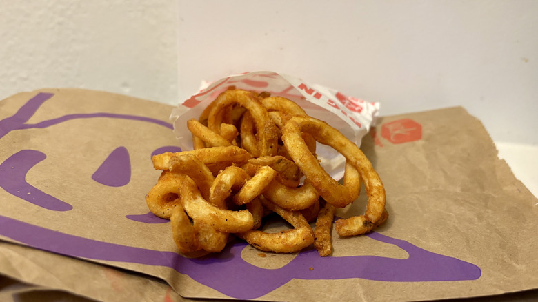 Curly fries sitting on a Jack in the Box bag