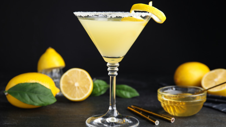 A Bees Knees cocktail on a table with with lemons and honey