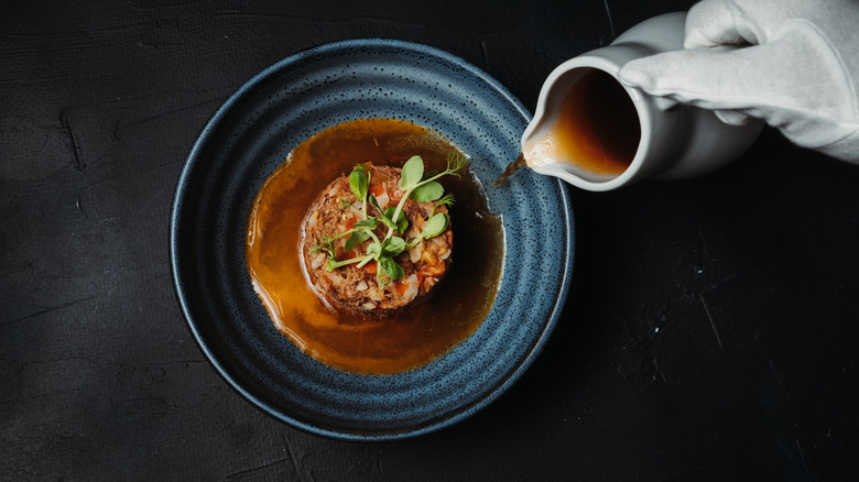 Person plating food with jug of sauce