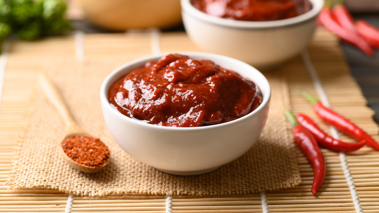 Bowl of gochujang paste on a bamboo mat, red chilis on the side