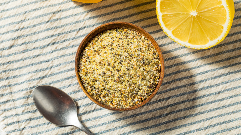 Bowl of lemon pepper seasoning on a cloth with a spoon and lemon half on the side