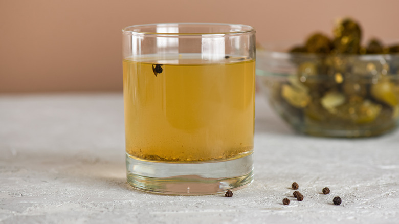 Glass of pickle juice with black peppercorns on the side