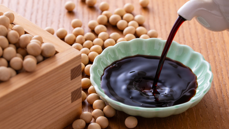 Soy sauce being poured into a small dish with soybeans on the side