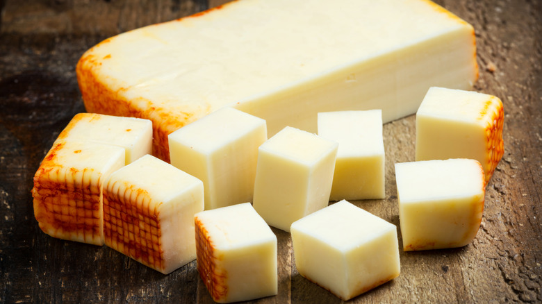 Large slice and cubed pieces of Muenster cheese on a brown wooden surface