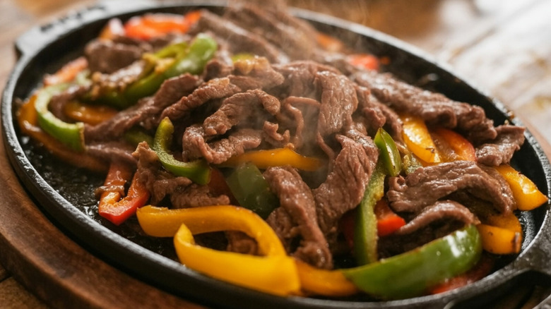 A close-up of smoking meat and veggies on a fajita skillet