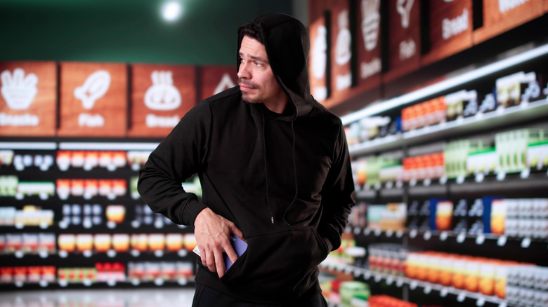 A man in a black hoodie stealing from a grocery store