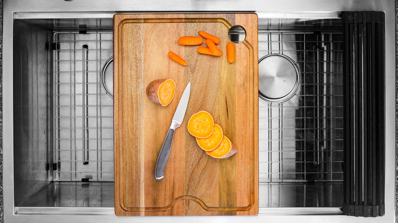 A wooden cutting board fitted over a kitchen sink