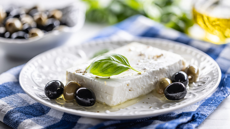 Block of feta cheese with olives and basil