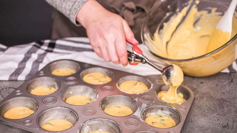 A woman filling a muffin tin with cornbread batter