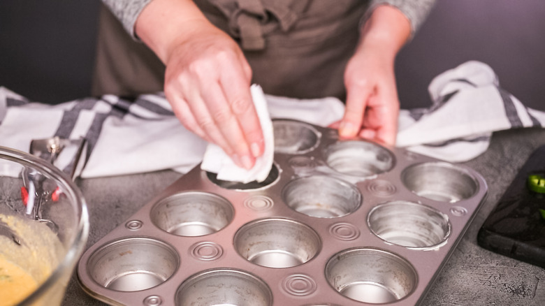 A woman greasing the inside of a muffin tin