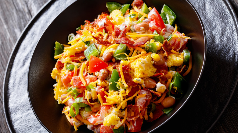 A black bowl of cornbread chunks with beans, tomatoes, peppers, and cheese mixed together