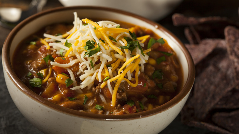 An offwhite bowl of chili with cheese and cilantro topping
