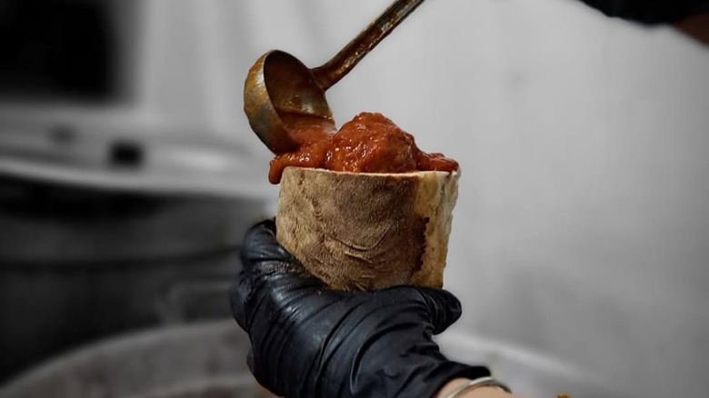 A person ladeling sauce into an Italian Cuzzetiello sandwich
