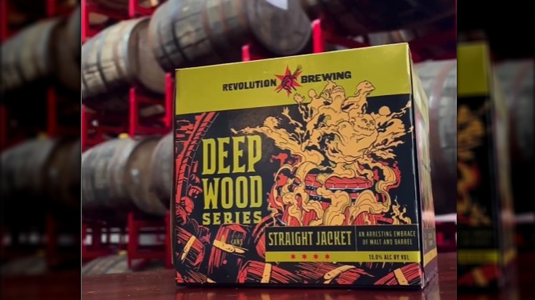 A case of Revolution Brewing Straight Jacket beer is in front of barrels.