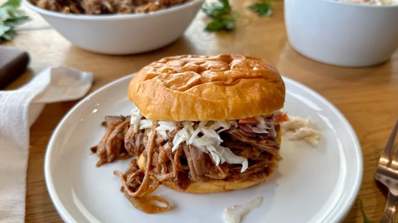 a pulled pork sandwich with coleslaw on a white plate