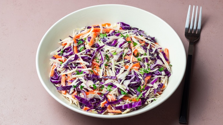 a bowl of prepared coleslaw with purple cabbage on a beige background