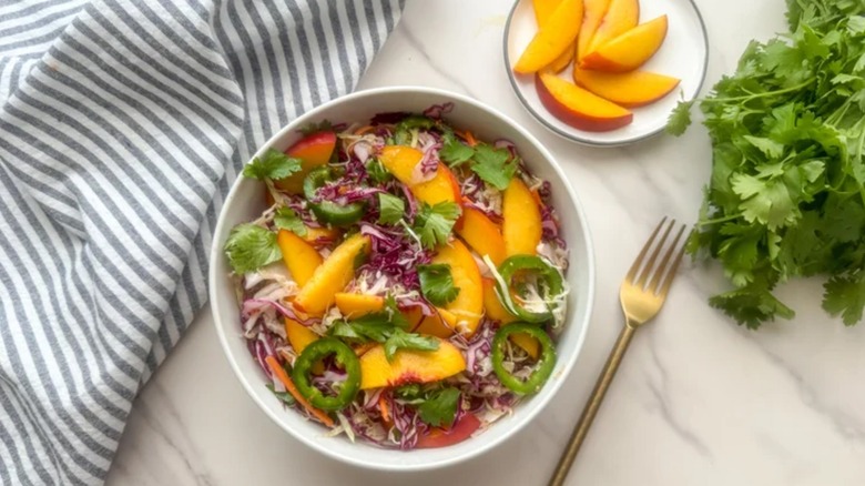 spicy peach coleslaw in a white bowl on a marble table