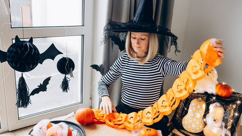 Person in witch hat holding pumpkin garland next to various Halloween decorations
