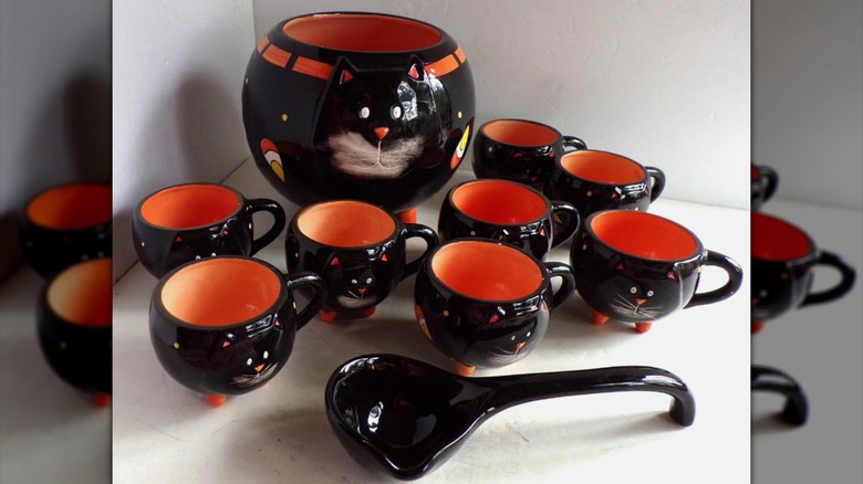 A large punch bowl shaped like a black cat, surrounded by smaller cat-shaped cups and a black ladle
