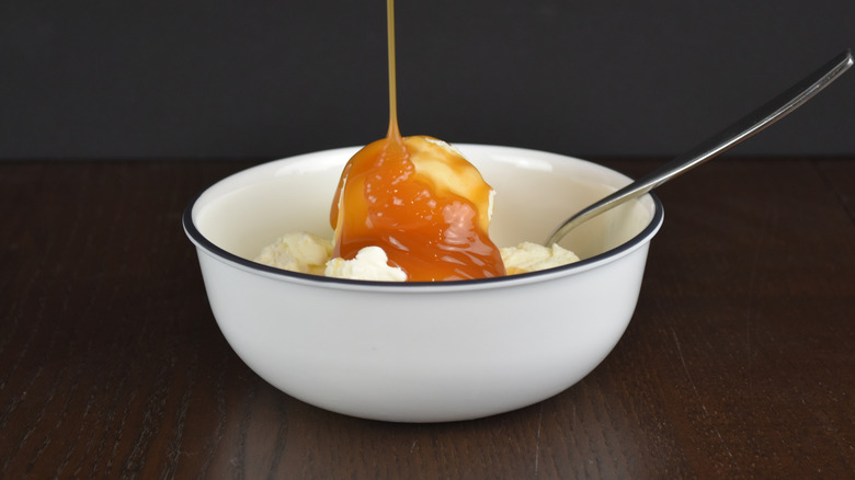 Caramel sauce is poured over ice cream in a bowl