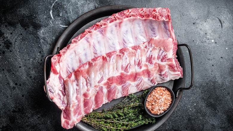 A plate of raw pork ribs with seasoning and herbs