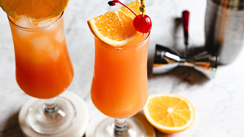 two hurricane cocktails on white marble background with bar tools