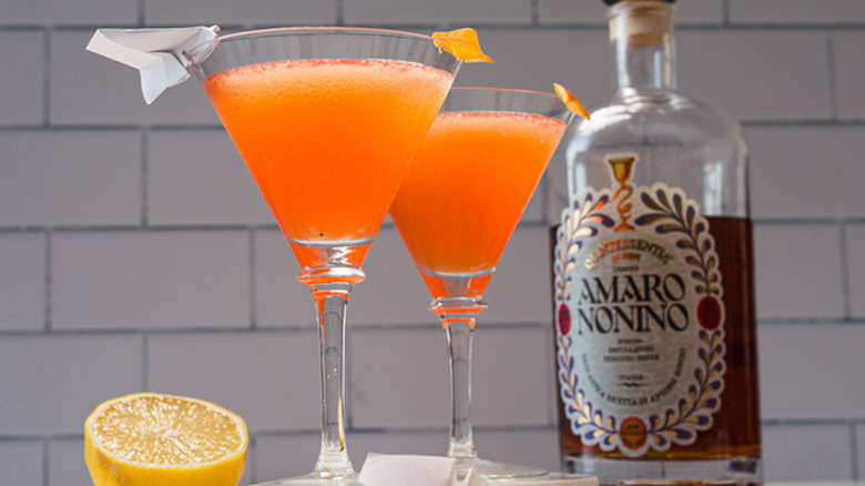 two paper plane cocktails in martini glasses with lemon and bottle of amaro nonino