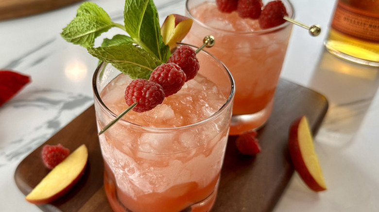 Peach And Raspberry Bourbon Smash on wooden cutting board
