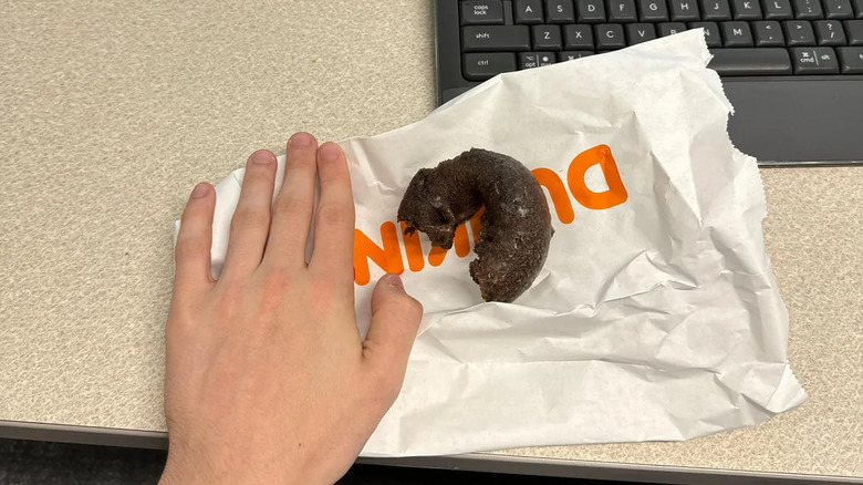 A Dunkin' donut on a paper bag next to a person's hand