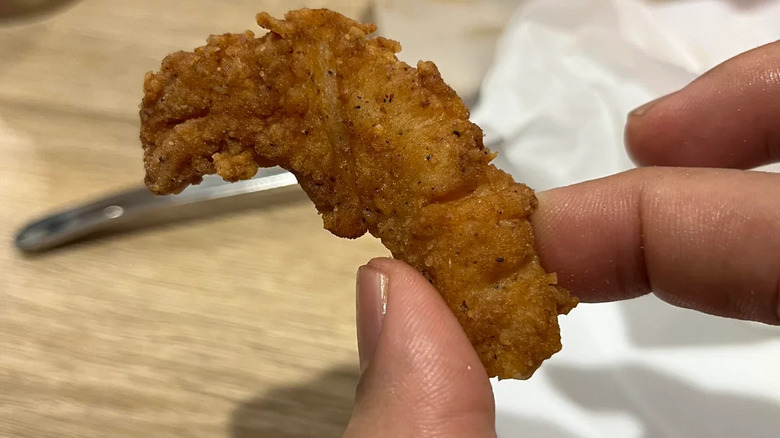 A person holding a chicken tender from KFC