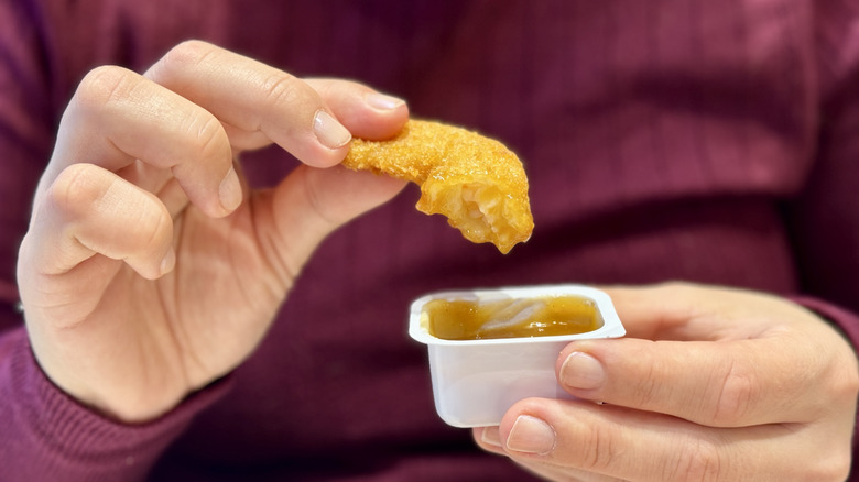 A person dipping a fast food chicken nugget into sauce